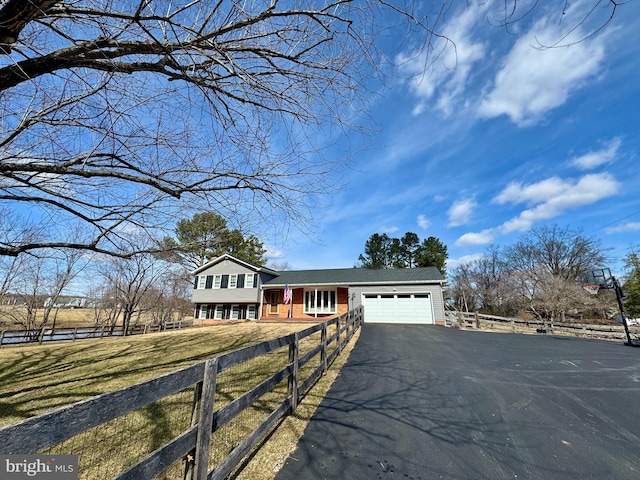 split level home featuring an attached garage, brick siding, fence, driveway, and a front lawn