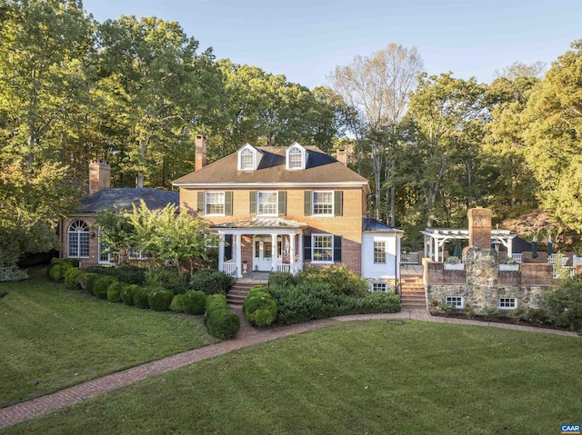 view of front of property with covered porch, a front lawn, a chimney, and brick siding