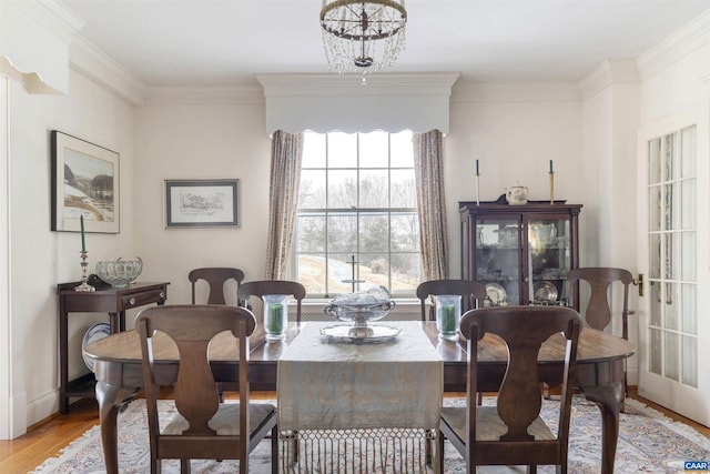 dining area with a notable chandelier, light wood-style floors, baseboards, and crown molding