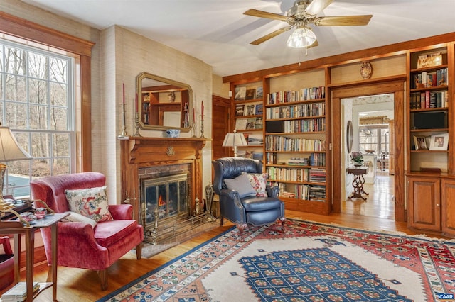 sitting room with a glass covered fireplace, ceiling fan, and wood finished floors