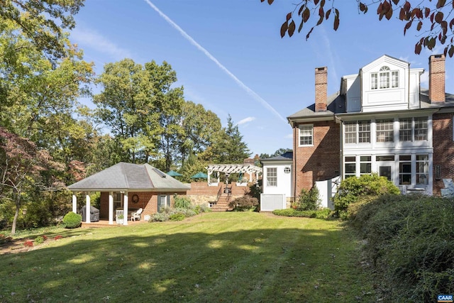 back of house featuring brick siding, a chimney, a lawn, and a pergola