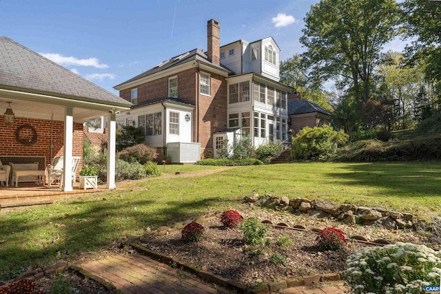 rear view of property with brick siding, a yard, and a chimney