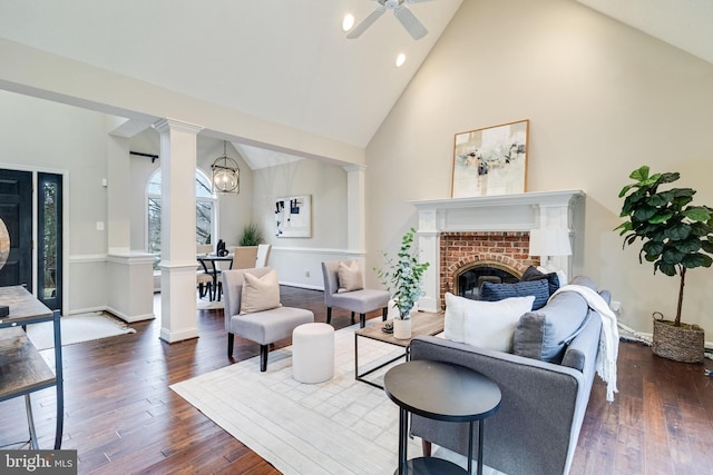 living room featuring dark wood-style floors, a brick fireplace, and decorative columns