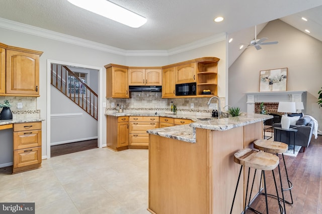 kitchen featuring light stone counters, a breakfast bar, under cabinet range hood, black microwave, and a sink