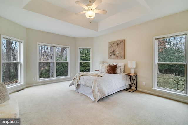 carpeted bedroom featuring a ceiling fan, a raised ceiling, visible vents, and baseboards