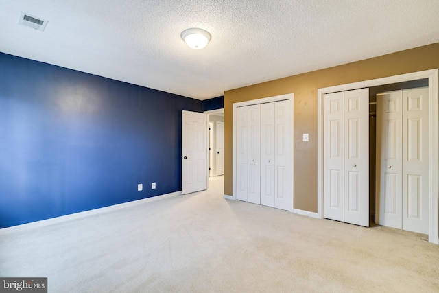 unfurnished bedroom featuring multiple closets, visible vents, carpet flooring, a textured ceiling, and baseboards