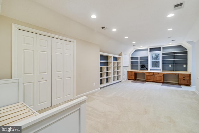 home office with lofted ceiling, built in shelves, light colored carpet, visible vents, and built in study area