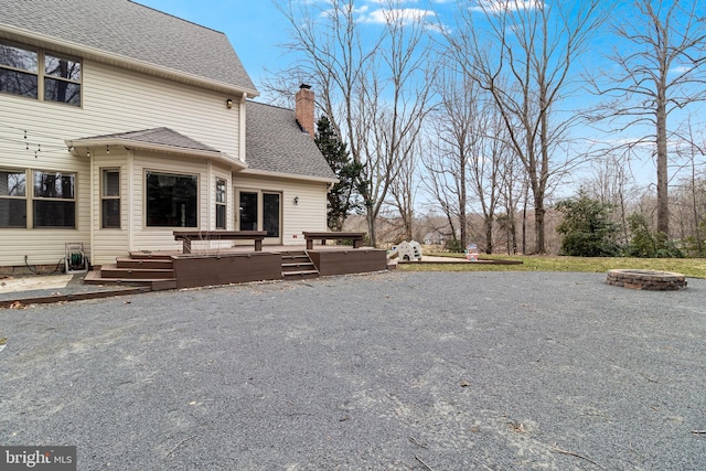 back of house featuring a deck, a chimney, roof with shingles, and a fire pit