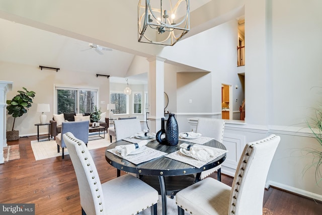 dining room featuring high vaulted ceiling, ceiling fan with notable chandelier, dark wood-style flooring, baseboards, and ornate columns