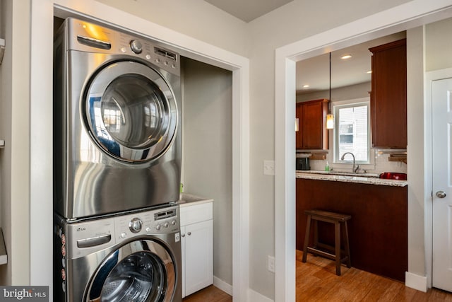 clothes washing area featuring recessed lighting, light wood-style flooring, stacked washer / dryer, a sink, and baseboards