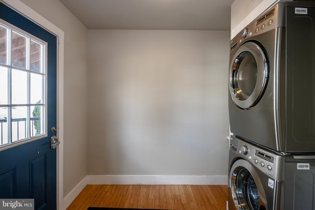 laundry room featuring laundry area, stacked washing maching and dryer, light wood-style flooring, and baseboards