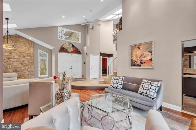 living room featuring a skylight, ceiling fan, wood finished floors, stairs, and high vaulted ceiling