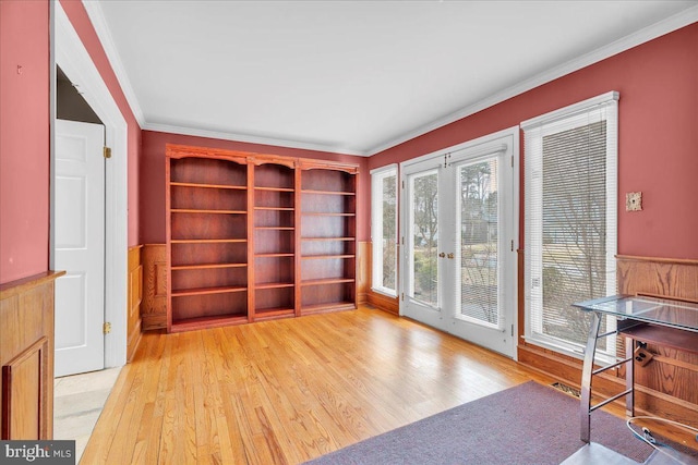 sitting room with a wainscoted wall, french doors, ornamental molding, and light wood-type flooring