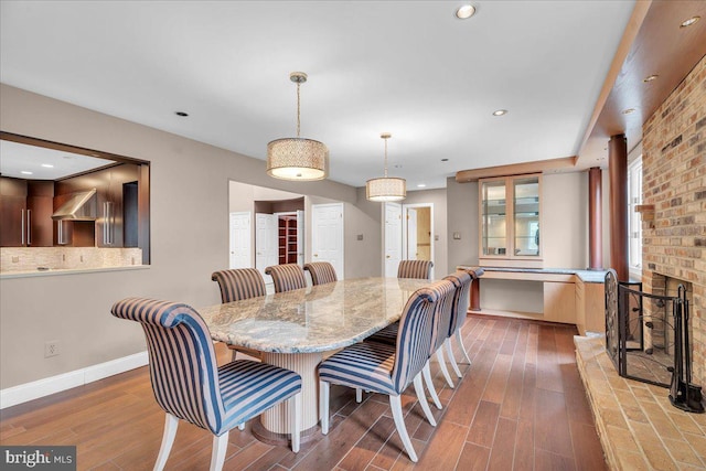 dining space featuring a brick fireplace, baseboards, wood finished floors, and recessed lighting