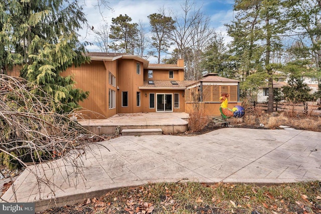 rear view of property featuring a chimney and a patio area