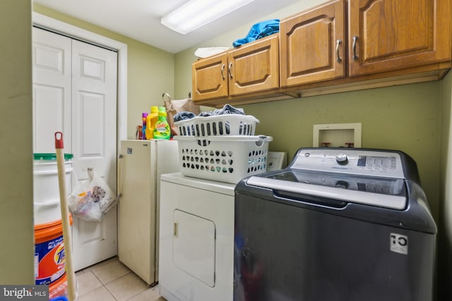 clothes washing area featuring separate washer and dryer, light tile patterned flooring, and cabinet space