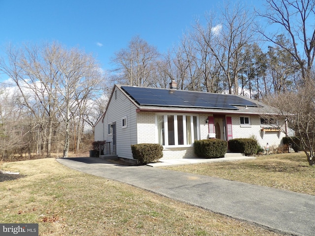 single story home featuring a front yard, brick siding, entry steps, and solar panels