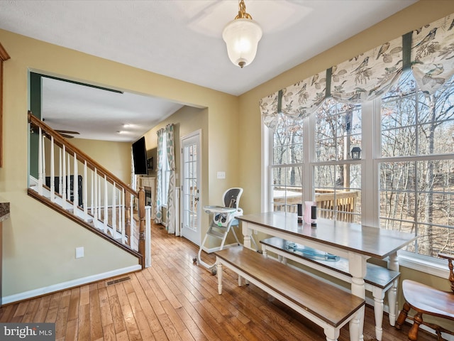 dining space with a fireplace, wood-type flooring, visible vents, stairway, and baseboards