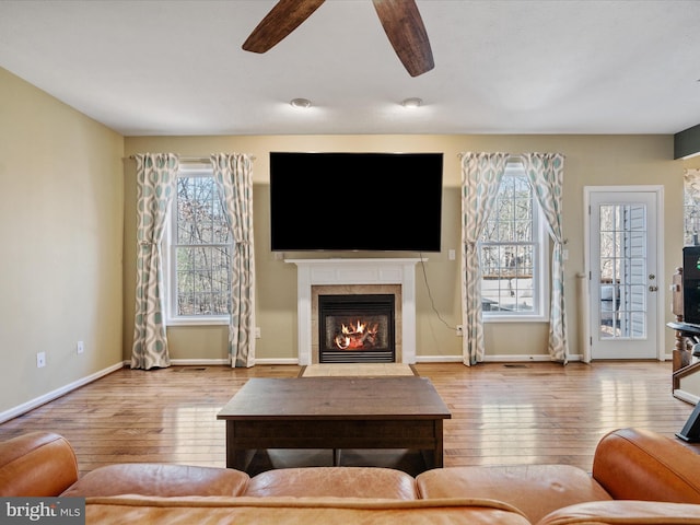 living room featuring ceiling fan, hardwood / wood-style floors, a glass covered fireplace, and baseboards