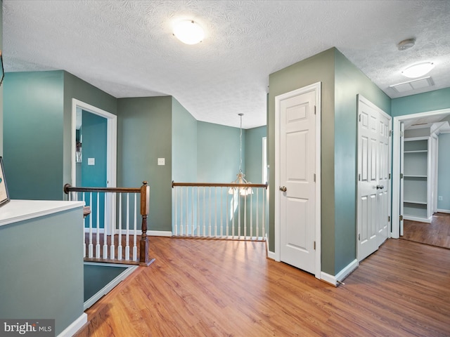 hallway with baseboards, visible vents, wood finished floors, and an upstairs landing