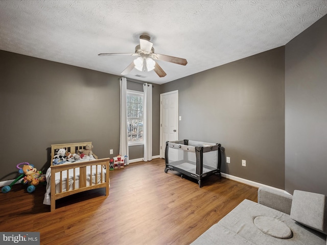 bedroom with a textured ceiling, wood finished floors, a ceiling fan, visible vents, and baseboards