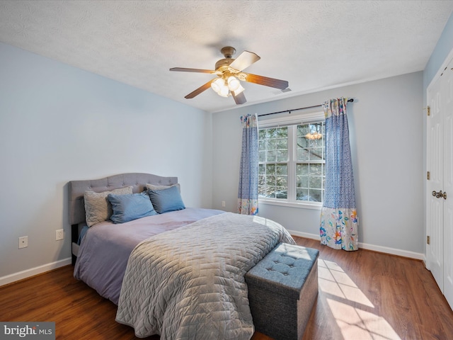 bedroom featuring ceiling fan, a textured ceiling, baseboards, and wood finished floors