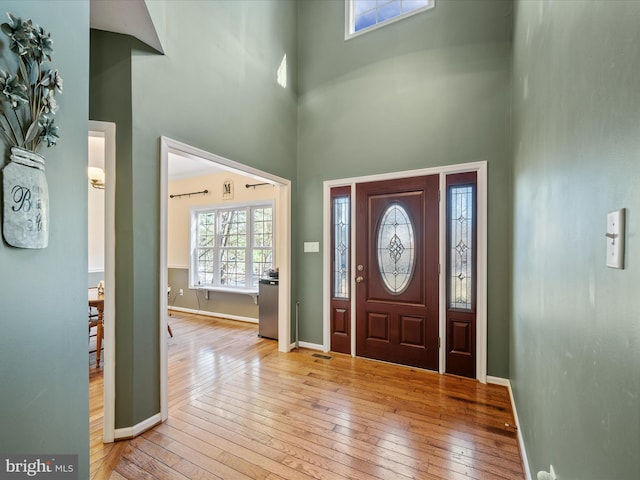 entryway featuring baseboards, light wood-style flooring, and a towering ceiling