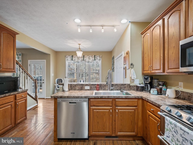 kitchen with brown cabinetry, appliances with stainless steel finishes, hardwood / wood-style floors, a peninsula, and a sink