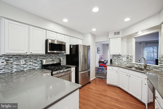 kitchen with visible vents, white cabinets, stainless steel appliances, light wood-type flooring, and a sink