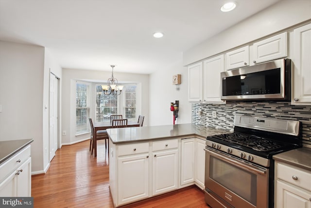 kitchen featuring stainless steel appliances, a peninsula, light wood finished floors, and tasteful backsplash