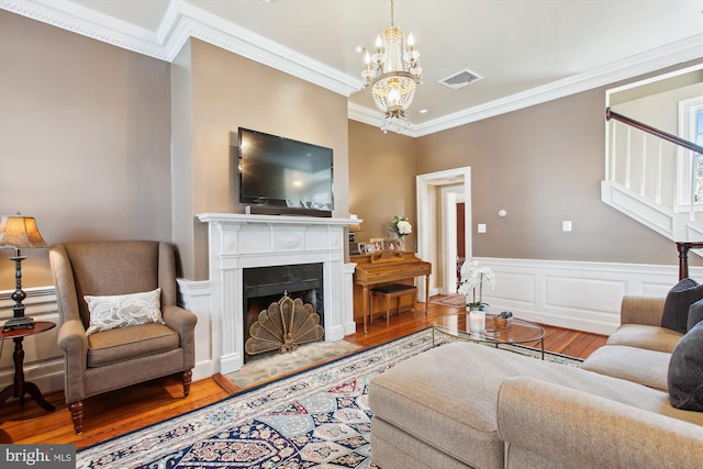 living room with visible vents, ornamental molding, an inviting chandelier, and wood finished floors