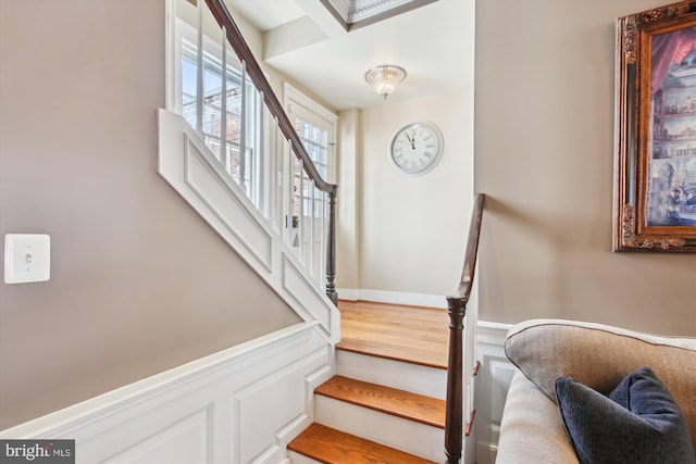 stairway with wood finished floors and wainscoting