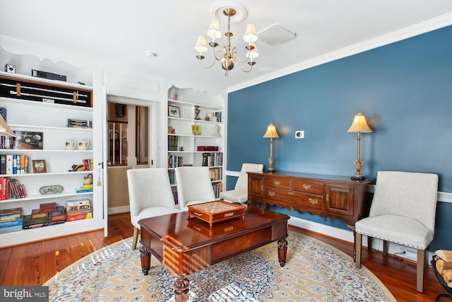 sitting room with built in features, a notable chandelier, wood finished floors, and ornamental molding