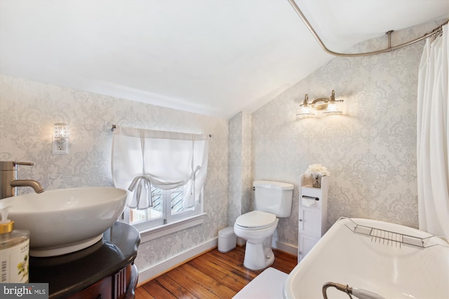 bathroom featuring a sink, wood finished floors, vaulted ceiling, and wallpapered walls