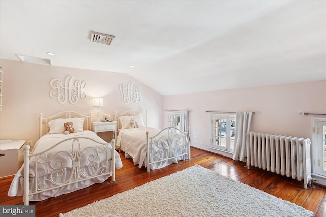 bedroom featuring visible vents, hardwood / wood-style flooring, radiator heating unit, and vaulted ceiling