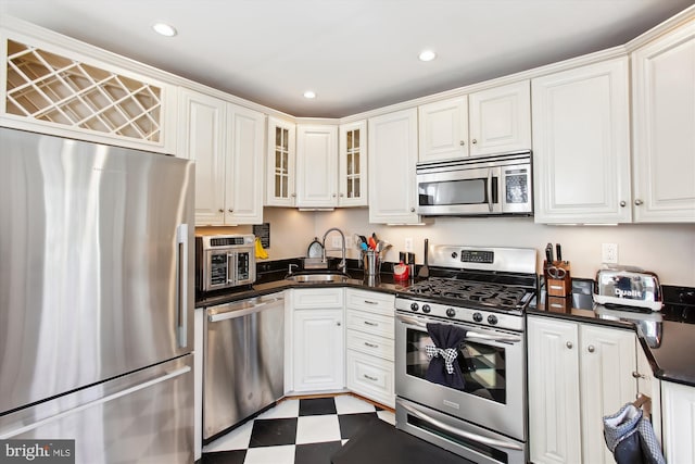 kitchen with tile patterned floors, a sink, dark countertops, white cabinetry, and stainless steel appliances