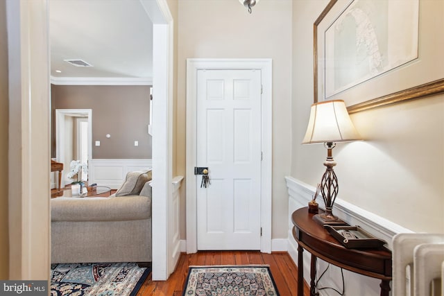 foyer featuring a wainscoted wall, wood finished floors, visible vents, and ornamental molding