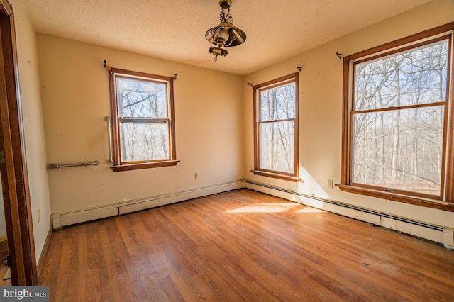 spare room with a textured ceiling, baseboard heating, plenty of natural light, and wood finished floors