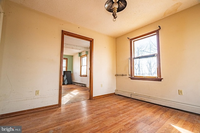 unfurnished room with a textured ceiling, baseboards, baseboard heating, and wood finished floors