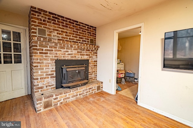 living room featuring a wood stove, visible vents, baseboards, and wood finished floors