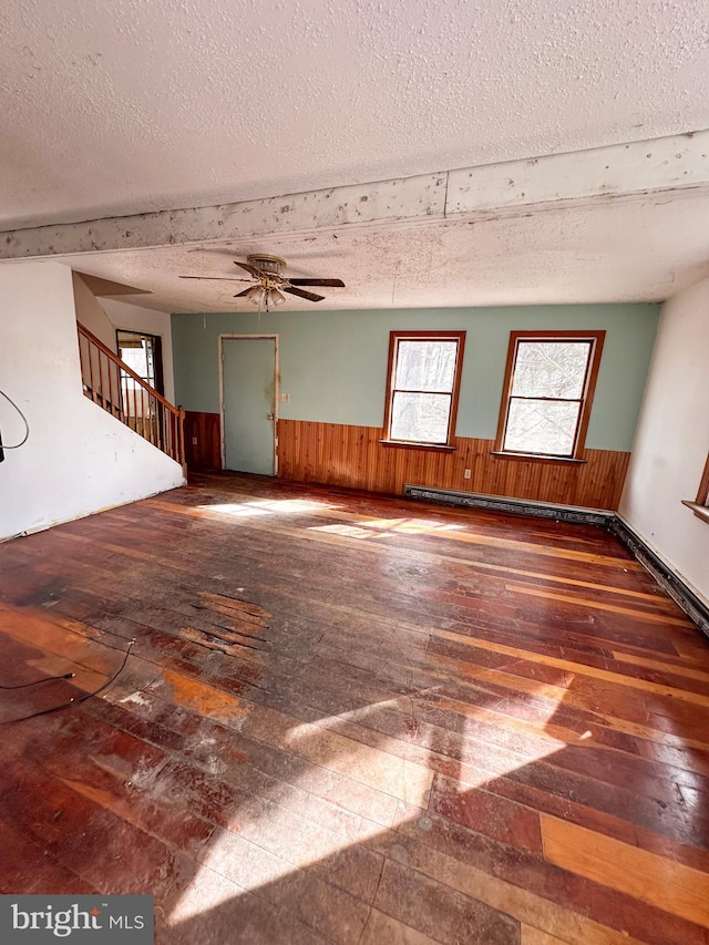 unfurnished living room with a textured ceiling, a wainscoted wall, wood walls, stairway, and hardwood / wood-style floors