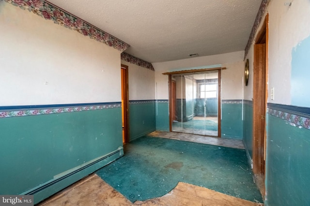 corridor with a wainscoted wall, a textured ceiling, and baseboard heating