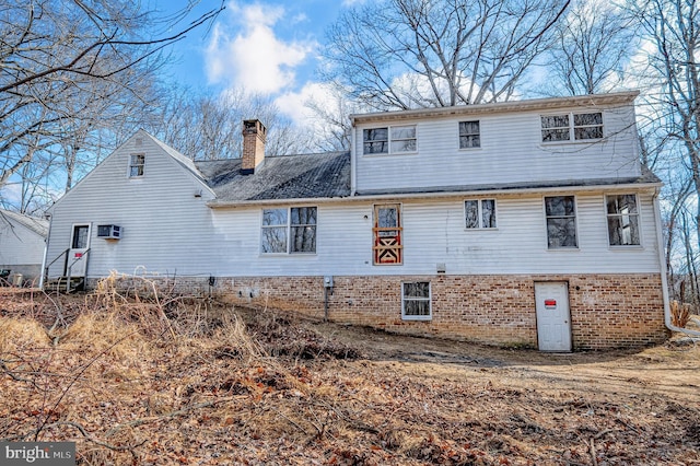 rear view of house with entry steps, brick siding, and a chimney