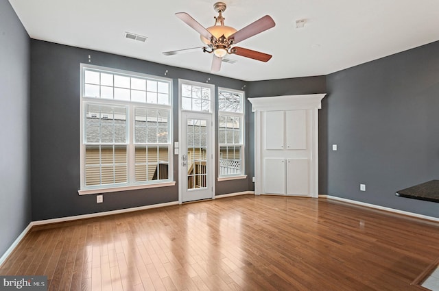 unfurnished room featuring a ceiling fan, baseboards, visible vents, and wood finished floors