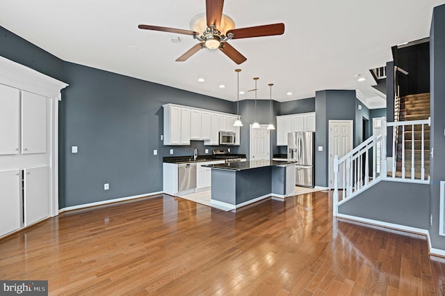 kitchen with dark countertops, appliances with stainless steel finishes, a center island, light wood-style floors, and white cabinetry