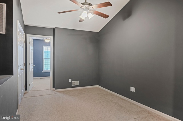 carpeted empty room with a ceiling fan, lofted ceiling, visible vents, and baseboards