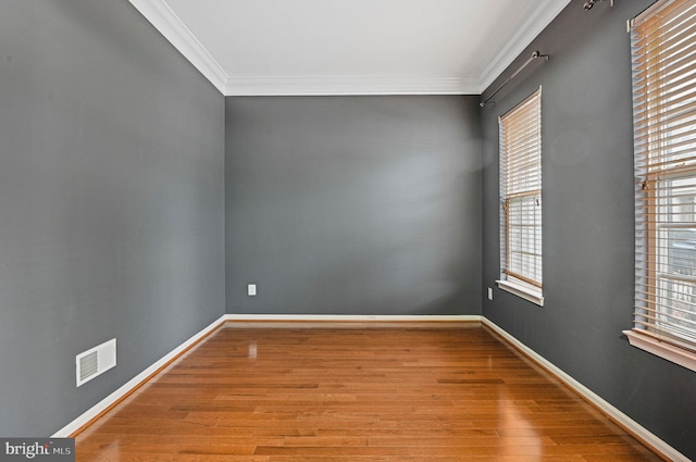 empty room featuring ornamental molding, visible vents, baseboards, and wood finished floors