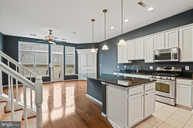 kitchen with stainless steel appliances, white cabinetry, a kitchen island, a sink, and ceiling fan