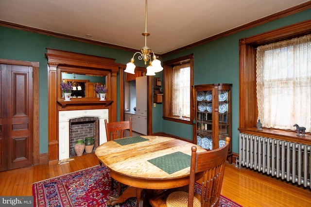 dining room featuring a chandelier, a fireplace, radiator, hardwood / wood-style floors, and crown molding