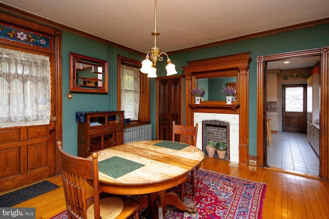 dining room with light wood-style floors, a chandelier, a fireplace, and crown molding